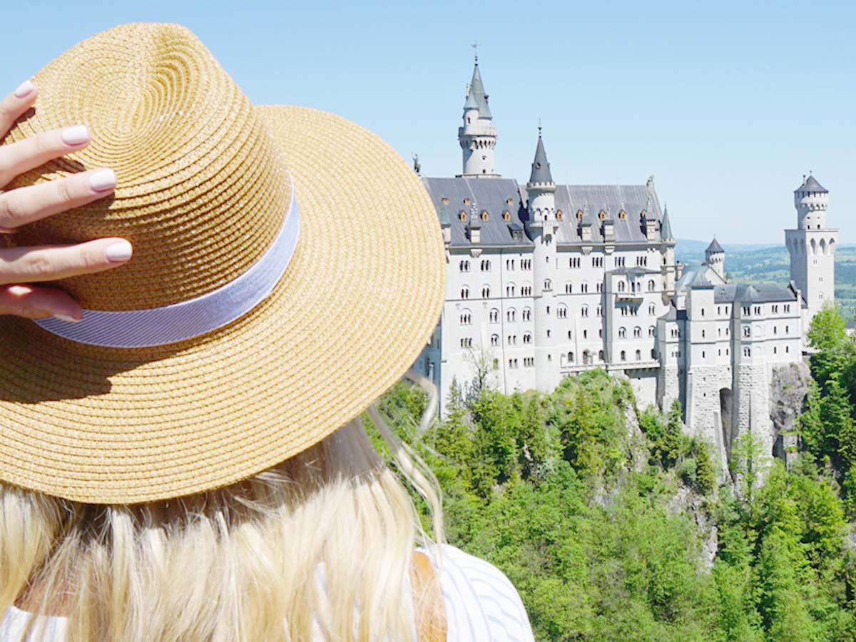 Blonde girl with hat looking at Neuschwanstein Castle from Marienbrucke
