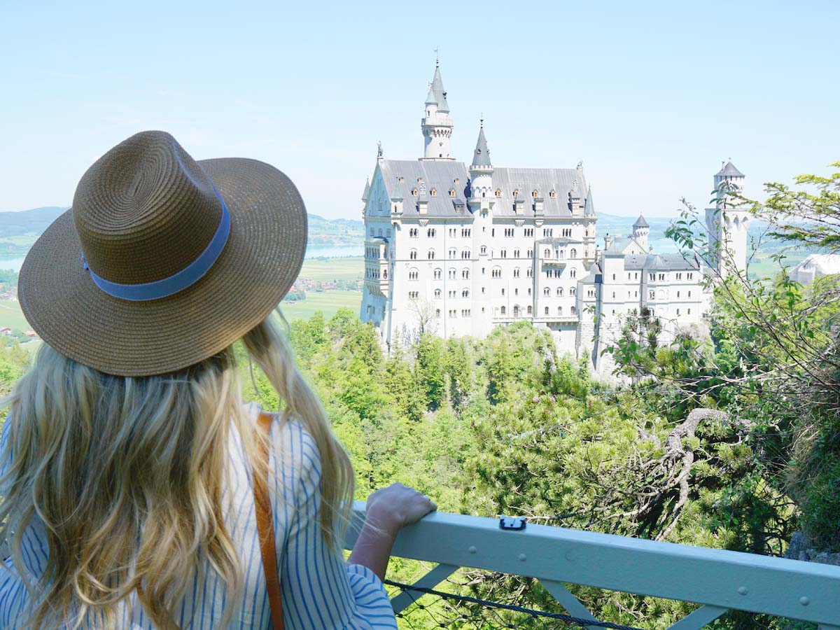 Blonde girl in hat looking at Neuschwanstein Castle from Marienbrucke