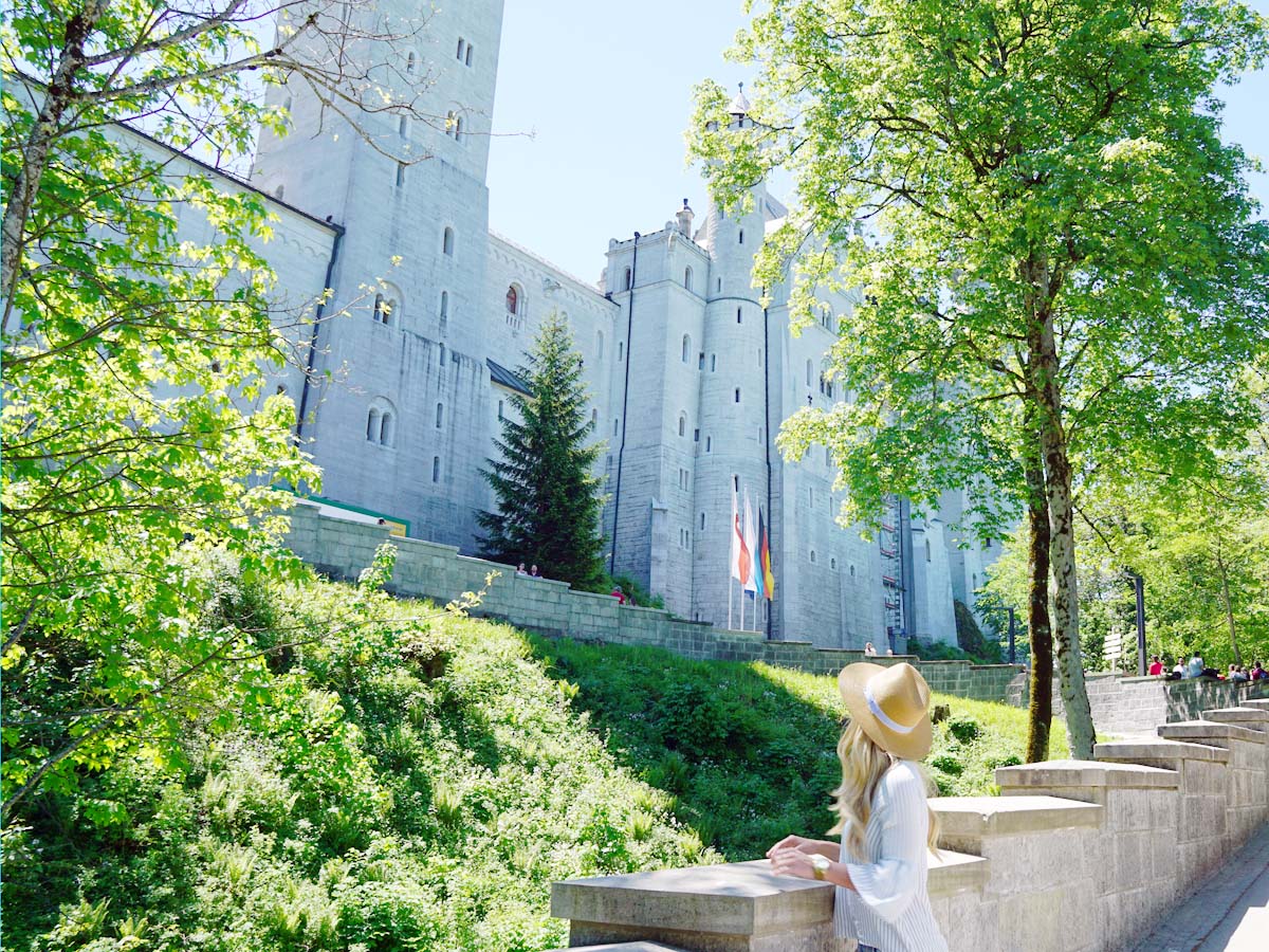 Blonde girl looking at Neuschwanstein Castle from bottom of the hill